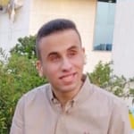 Young Egyptian man with short hair and a tan shirt, smiles
